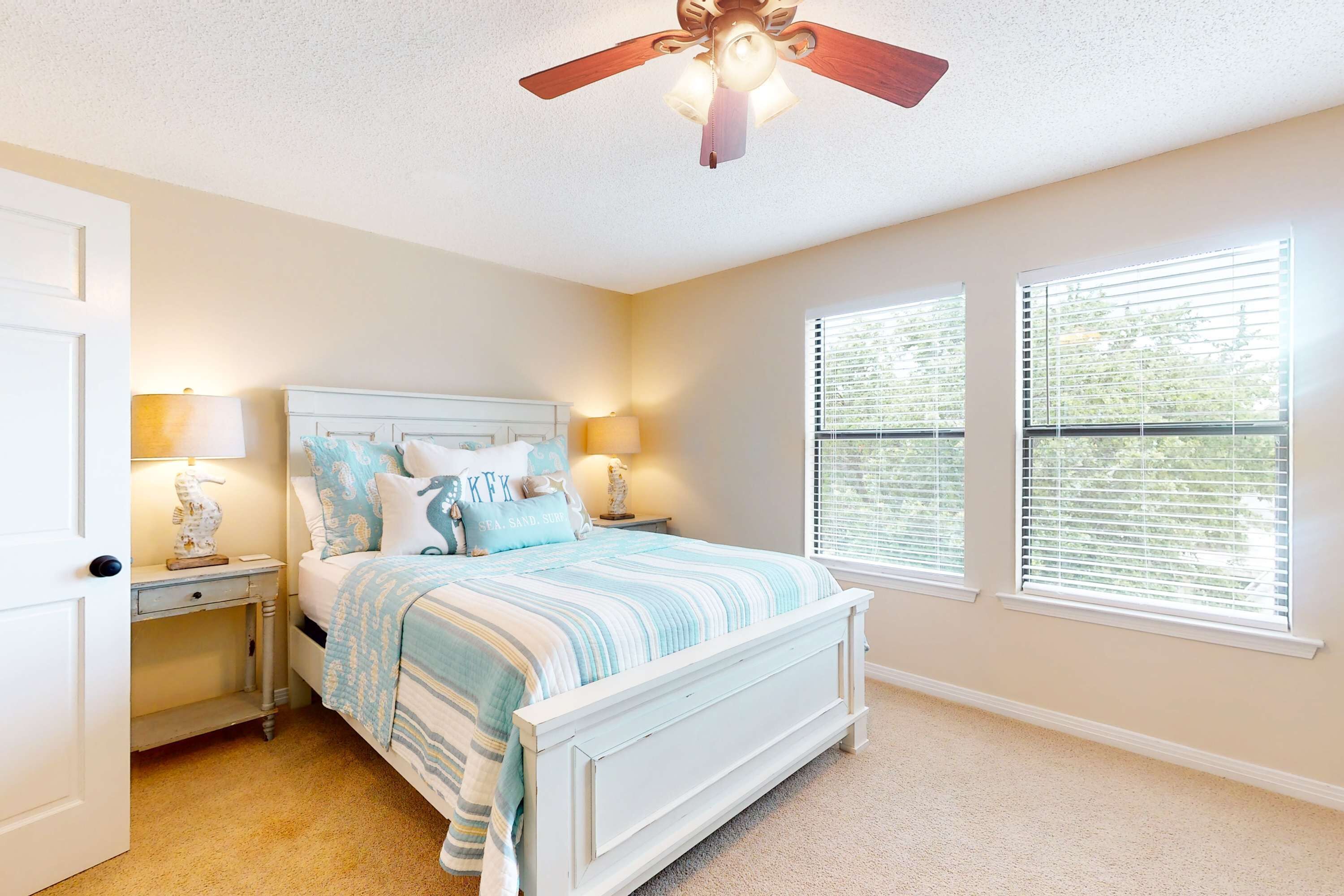 A bedroom with a bed, nightstands, lamps, a ceiling fan, and two windows with blinds.
