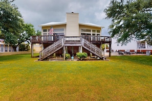 A two-story building with a central staircase, a flag, and a small garden area. - Bayfront home with boat dock, water views, deck, & fish cleaning station (Dauphin Island)