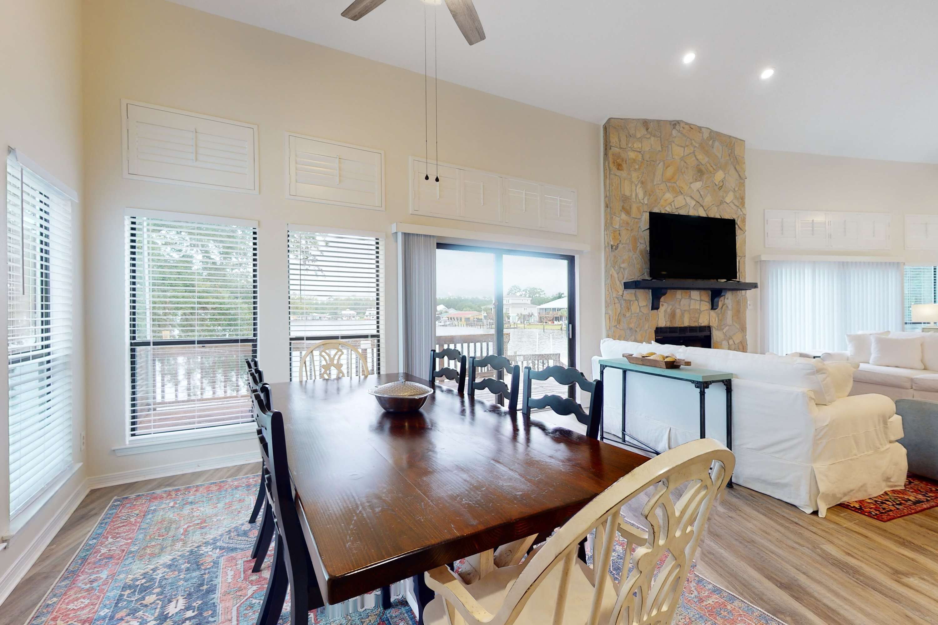 A dining area with a wooden table, chairs, and a bowl. There is a stone wall with a flat-screen TV.