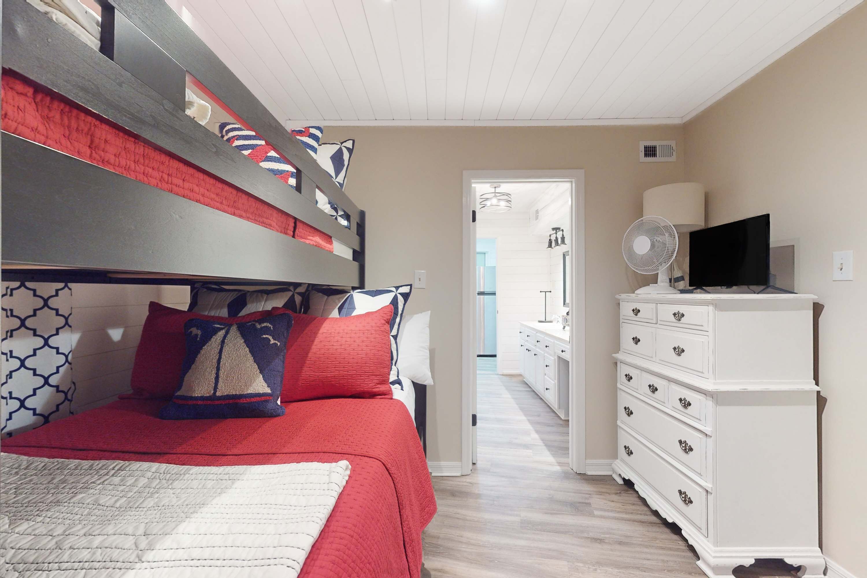 A bedroom with a bunk bed, a dresser, a TV, and a fan.