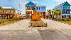 A beachfront building with a wooden staircase leading to a deck, surrounded by palm trees and a clear sky. - Cadillac Margarita, House in Dauphin Island (Dauphin Island)