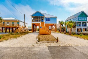 Ein Gebäude direkt am Strand mit einer Holztreppe, die zu einer Terrasse führt, umgeben von Palmen und einem klaren Himmel.
