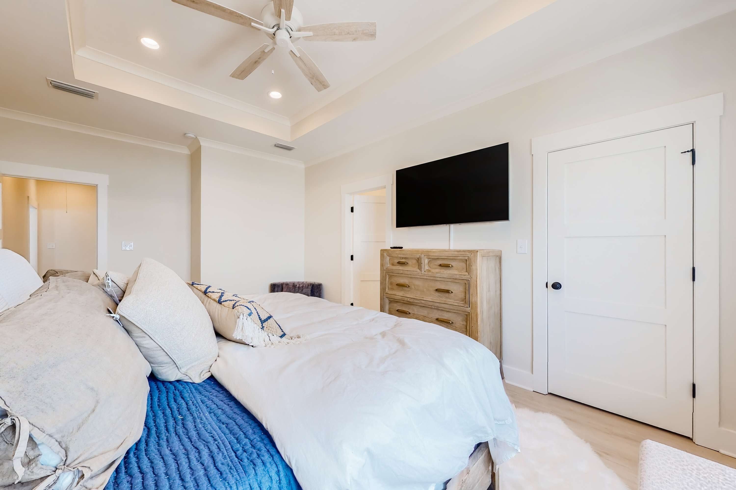 A bedroom with a bed, a ceiling fan, a TV, a dresser, and a door.