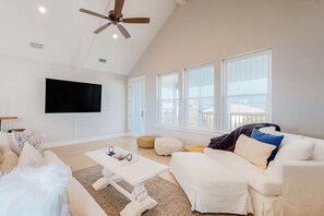 Ein geräumiges Wohnzimmer mit Deckenventilator, Flachbildfernseher und großen Fenstern.
