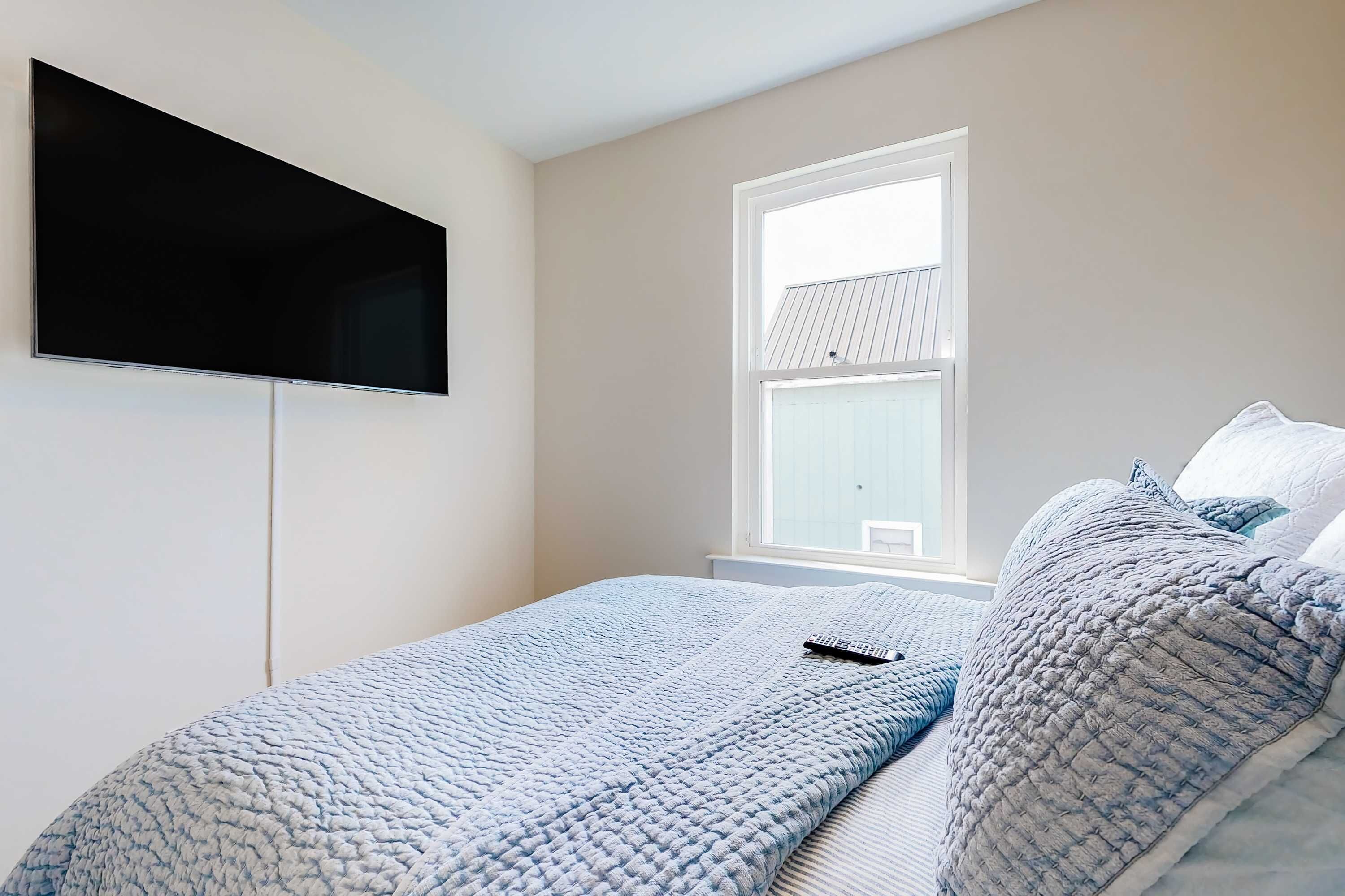 A bedroom with a bed, a TV mounted on the wall, and a window.