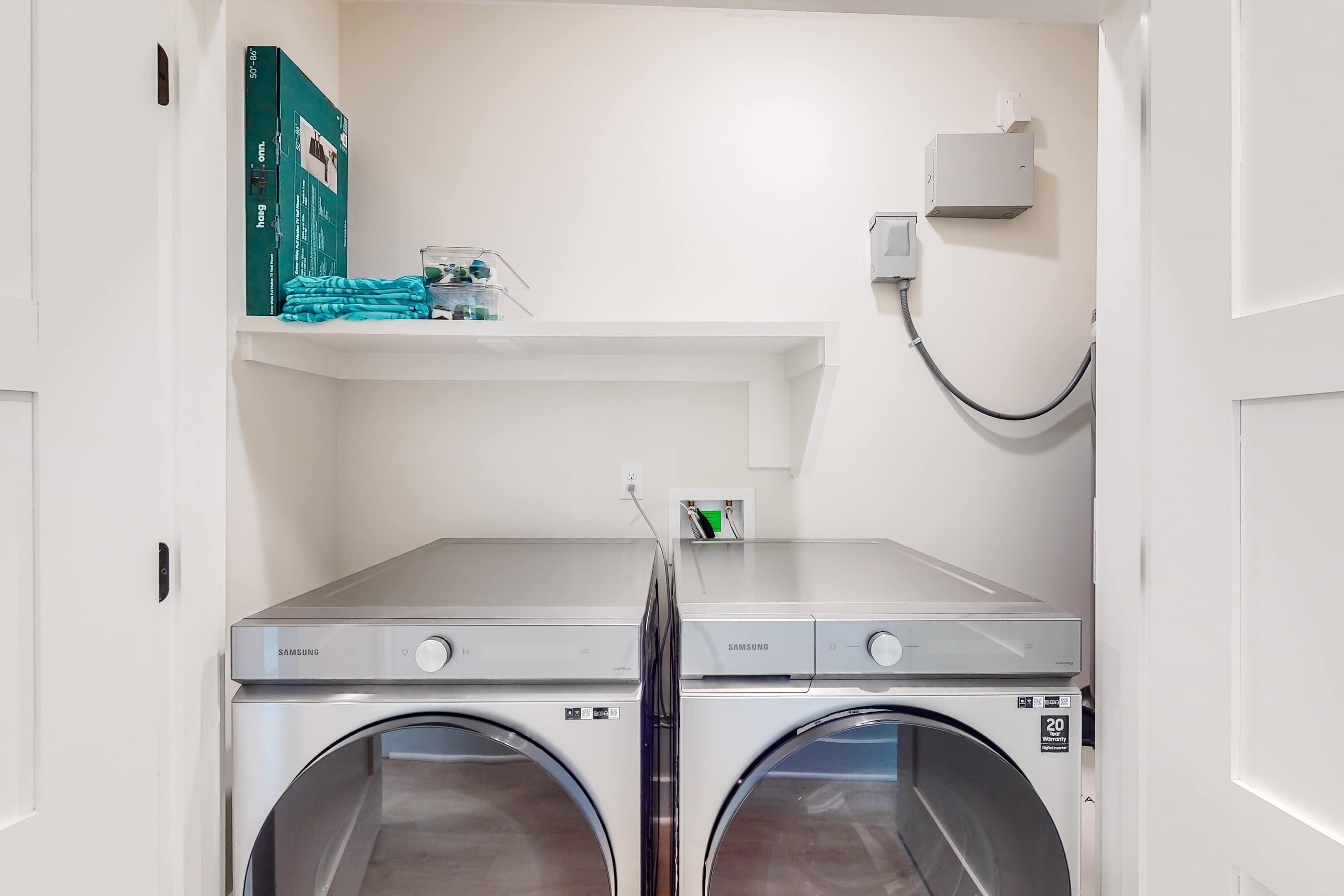 A laundry area with two Samsung washing machines, a shelf with toiletries, and a wall-mounted heater.