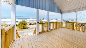 A covered outdoor deck with wooden railings and a view of houses and a tree. - Cadillac Margarita, House in Dauphin Island (Dauphin Island)