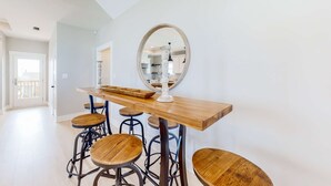 A modern kitchen with a wooden bar and stools, a large mirror, and a view into the dining area. - Cadillac Margarita, House in Dauphin Island (Dauphin Island)