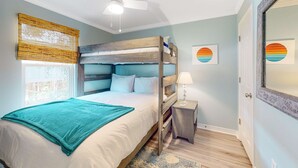 Un dormitorio con literas, ventilador de techo, mesita de noche con lámpara y una obra de arte en la pared.