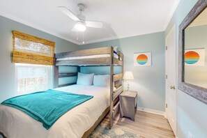 Ein Schlafzimmer mit einem Etagenbett, einem Deckenventilator, einem Nachttisch mit Lampe sowie Bildern an der Wand.