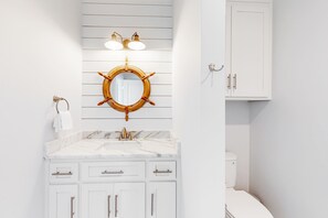 Ein Badezimmer mit weißem Waschtisch, einem runden Spiegel im Schiffsschrauben-Design und einer weißen Toilette.