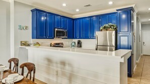 A modern kitchen with blue cabinets, a white countertop, and stainless steel appliances. - Perfect beachfront condo with pool, internet, and washer and dryer (Dauphin Island)