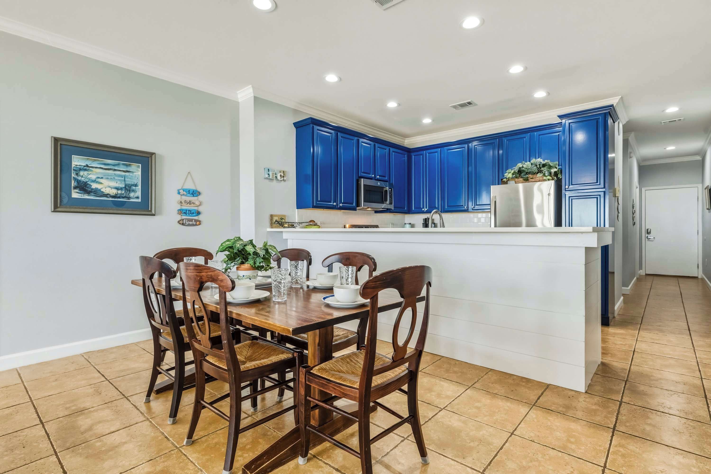 Une cuisine avec des meubles bleus, un îlot central blanc et un coin repas avec des chaises et une table en bois.