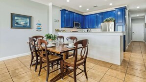 A kitchen with blue cabinets, a white island, and a dining area with wooden chairs and a table. - Perfect beachfront condo with pool, internet, and washer and dryer (Dauphin Island)