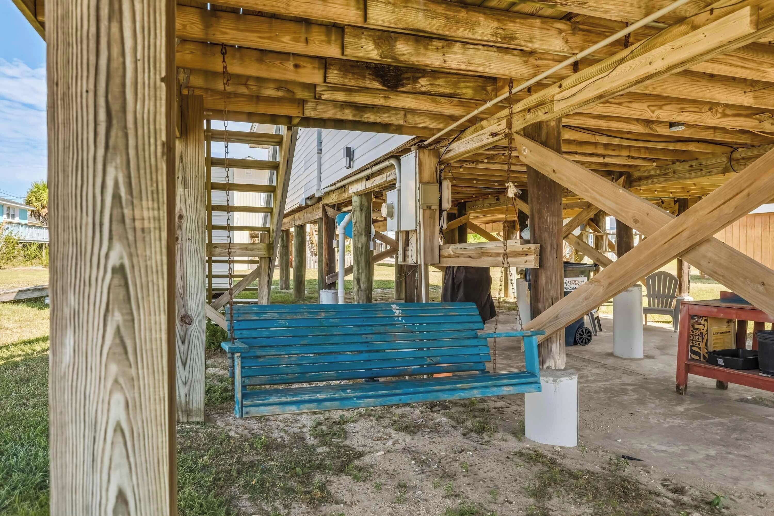 A wooden structure with a blue bench under a roof, surrounded by a grassy area.