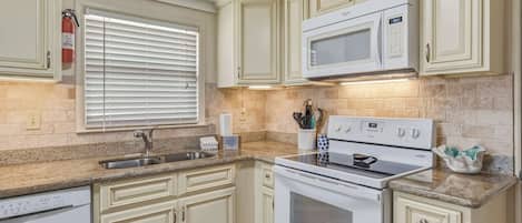 Cocina con armarios blancos, microondas, horno y lavaplatos.