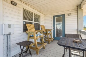 A covered porch with wooden chairs and a table, a door with a window, and an electrical box on the wall. - Dog-friendly house on Dauphin Island, Near beach access, Patio, Grill, Washer & Dryer (Dauphin Island)