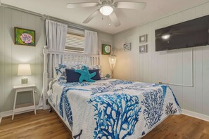 A bedroom with a bed, a nightstand, a lamp, a ceiling fan, a TV, and artwork on the walls. - Dog-friendly house on Dauphin Island, Near beach access, Patio, Grill, Washer & Dryer (Dauphin Island)