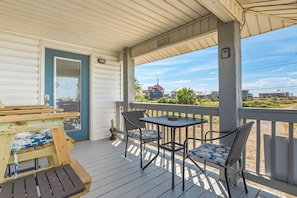 A covered porch with a table and chairs, a door, and a view of the surrounding area. - Dog-friendly house on Dauphin Island, Near beach access, Patio, Grill, Washer & Dryer (Dauphin Island)