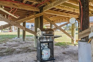 Een draagbare gasgrill onder een houten constructie, met zichtbare leidingen.