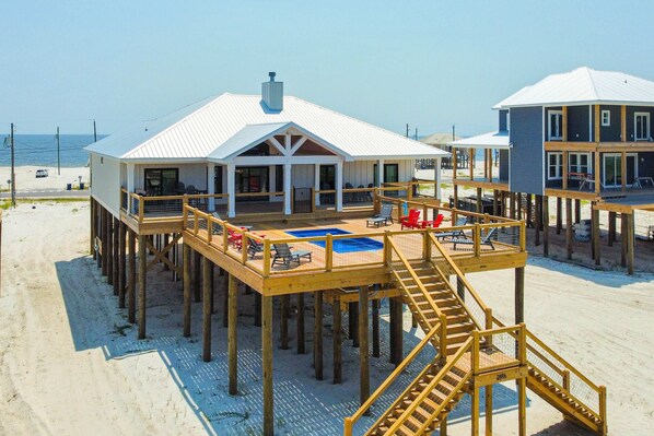 A beachfront property with a wooden deck, a pool, and a covered seating area. - Dog-friendly home with water views & private heated pool (Dauphin Island)