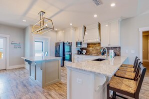 A modern kitchen with white cabinetry, a marble countertop, and a built-in island with seating. - Dog-friendly home with water views & private heated pool (Dauphin Island)