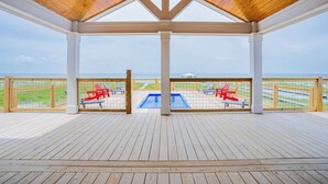 Um deck coberto com teto de madeira, piscina e cadeiras vermelhas.