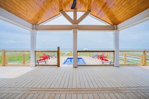 A covered deck with a wooden ceiling, a pool, and red chairs. - Dog-friendly home with water views & private heated pool (Dauphin Island)