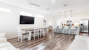 A modern kitchen with white cabinets, a stainless steel refrigerator, and a dining area with a wooden table and white chairs. - Coastal dog-friendly home with grill, balcony, & patio - short walk to the beach (Dauphin Island)