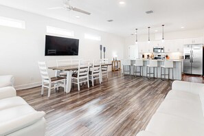 A modern kitchen with white cabinets, a stainless steel refrigerator, and a dining area with a wooden table and white chairs. - Coastal dog-friendly home with grill, balcony, & patio - short walk to the beach (Dauphin Island)