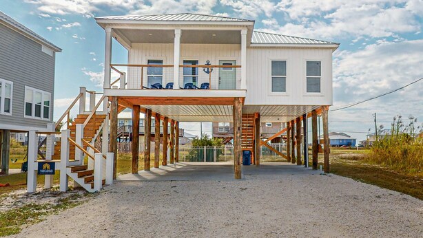 A two-story house with a covered porch and a staircase leading to the upper level. - Coastal dog-friendly home with grill, balcony, & patio - short walk to the beach (Dauphin Island)