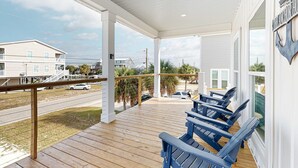 A covered porch with wooden flooring, blue Adirondack chairs, and a view of the street. - Coastal dog-friendly home with grill, balcony, & patio - short walk to the beach (Dauphin Island)