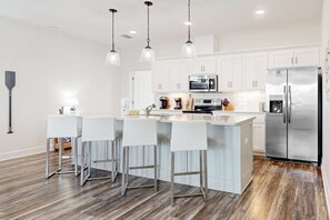 A modern kitchen with white cabinets, stainless steel appliances, and a central island with bar stools. - Coastal dog-friendly home with grill, balcony, & patio - short walk to the beach (Dauphin Island)