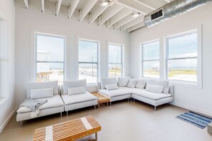 Una sala de estar moderna con sofás blancos, ventanas amplias y vista al mar.