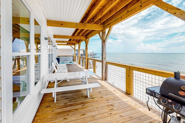 Una terraza de madera con sillones blancos y una parrilla, con vista al océano.
