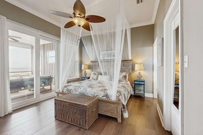 Ein Schlafzimmer mit Bett, Deckenventilator, Nachttisch, Weidenkorb und Blick durch ein Fenster.
