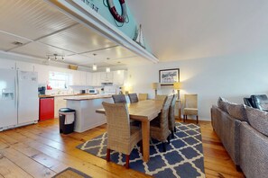 Una cocina moderna con armarios blancos, un lavavajillas rojo y una zona de comedor con mesa de madera y sillas de mimbre.
