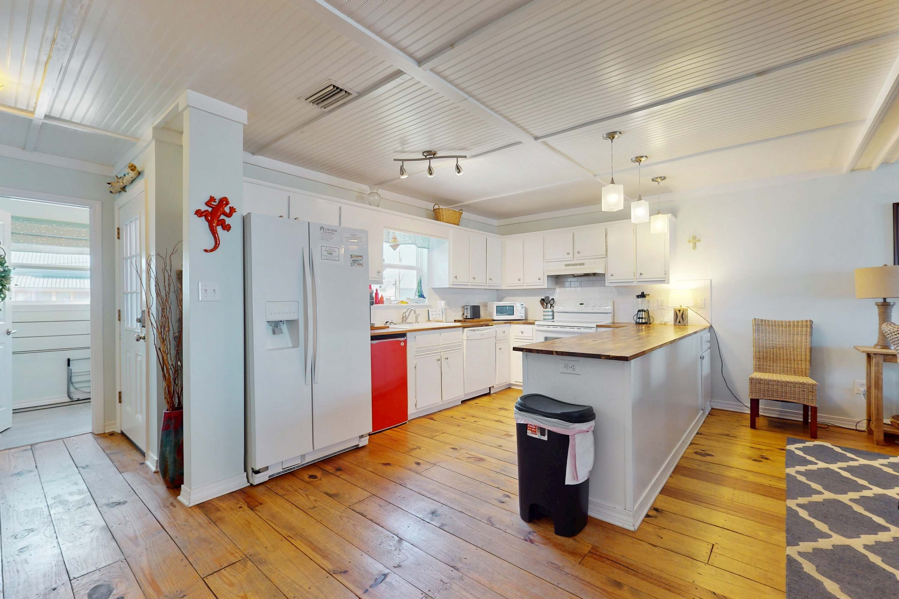 Una cocina moderna con armarios blancos, un refrigerador rojo, piso de madera y una pequeña isla con un basurero.