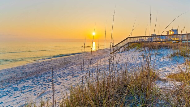 Ein Strand mit einer Holzpromenade, die zu einem Gebäude führt.