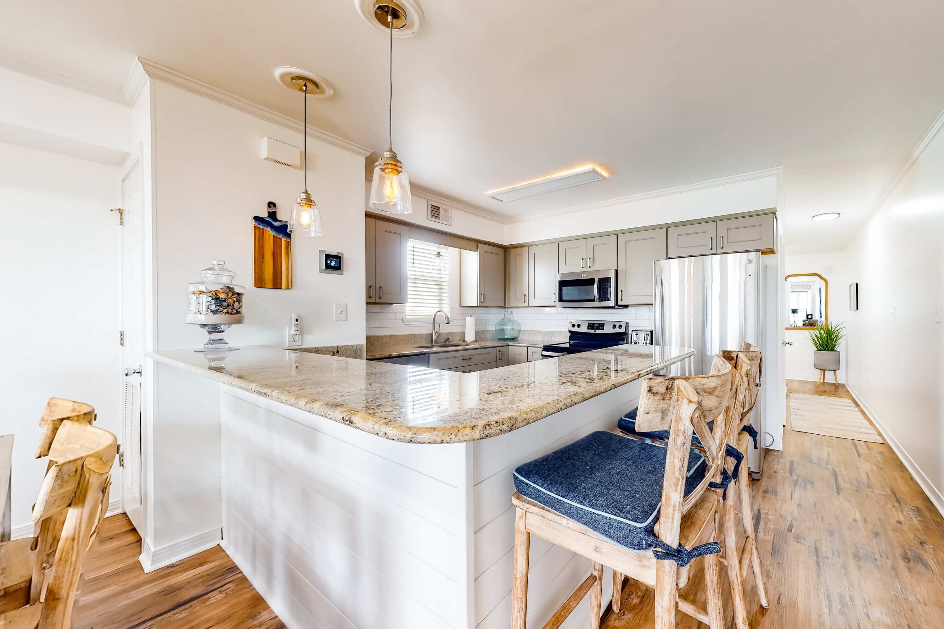 Cozinha moderna com ilha central, cadeiras de madeira e iluminação pendente.