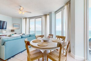 A room with a round wooden table, blue sofa, and a ceiling fan. - Beachfront Condo with Gulf View & Shared Pools & Hot Tubs - Snowbirds Welcome (Gulf Shores)