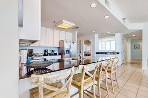 A modern kitchen with white cabinets, a central island with bar stools, and a large window providing natural light. - Beachfront Condo with Gulf View & Shared Pools & Hot Tubs - Snowbirds Welcome (Gulf Shores)