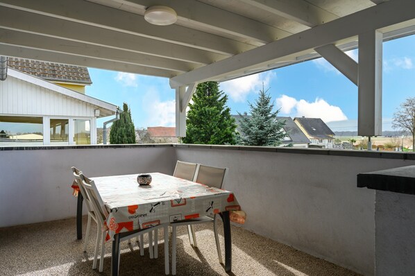 An outdoor patio with a table and chairs, a pergola, and a view of houses and trees.