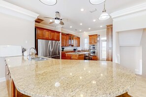 A kitchen with granite countertops, stainless steel appliances, wooden cabinets, and a ceiling fan. - Large and Beautiful Beachfront Home with Private Pool, Central AC (Gulf Shores)