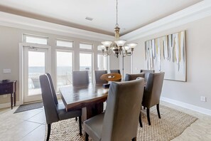 A dining room with a large table, six chairs, a chandelier, and a large window with a view. - Large and Beautiful Beachfront Home with Private Pool, Central AC (Gulf Shores)