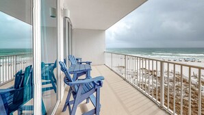 A balcony with a view of the beach and ocean, featuring blue chairs and a glass door. - Coastal Condo w Balcony & Shared Pools, Hot Tubs, Gym and Gulf views (Gulf Shores)