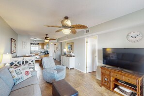 A living room with a TV, a ceiling fan, a dining area, and a kitchen. - Tropically decorated condo in gulf-side complex w/shared pool, central AC, WiFi (Gulf Shores)