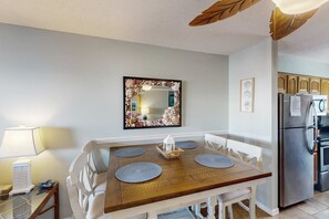 A dining area with a wooden table, white chairs, and a decorative mirror. - Tropically decorated condo in gulf-side complex w/shared pool, central AC, WiFi (Gulf Shores)