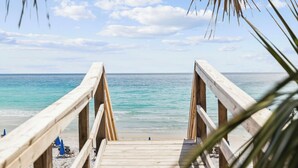 A wooden deck leading to a beach with clear turquoise water and a few people in the distance. - Sandpiper's Retreat|Gulf Front|Private Pool|Golf Cart (Santa Rosa Beach)