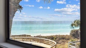 A view of a beach from a window with a wooden railing and a palm tree. - Sandpiper's Retreat|Gulf Front|Private Pool|Golf Cart (Santa Rosa Beach)